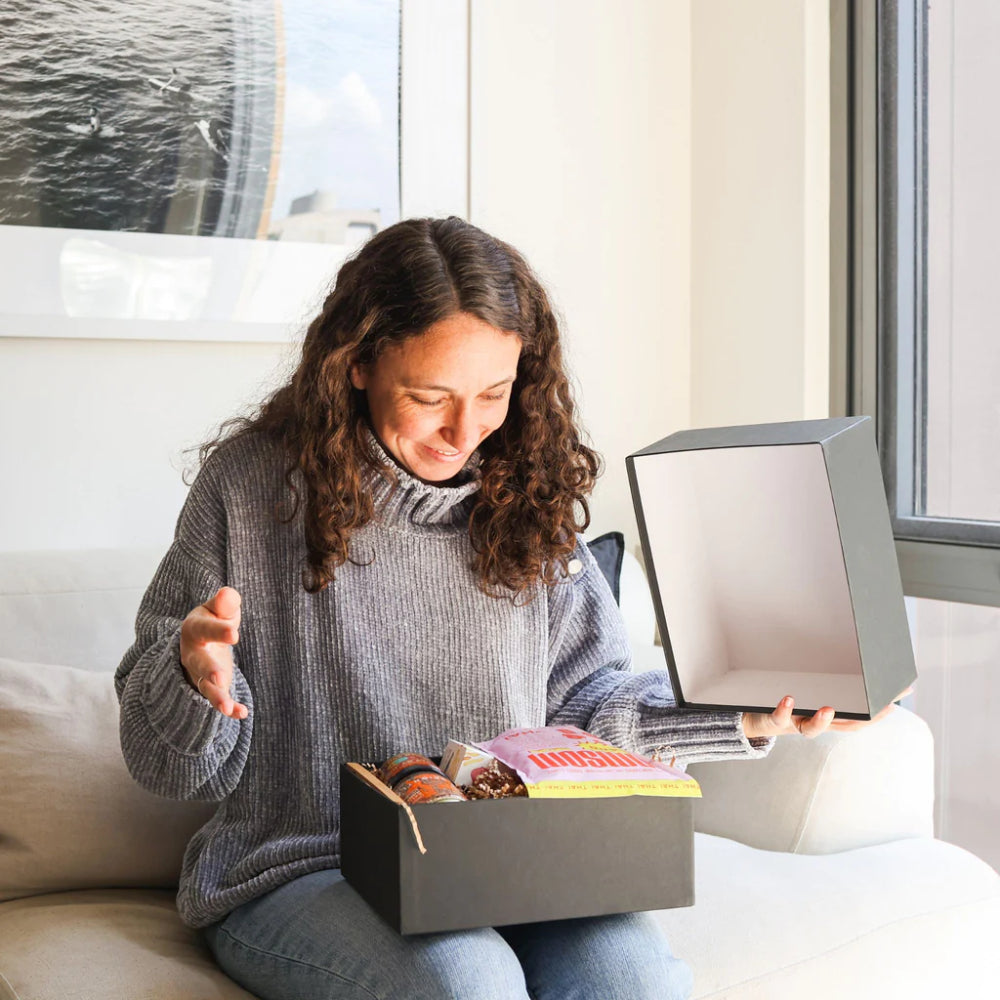 A woman sitting on a couch opening a box of food