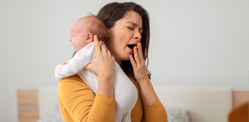 Tired young mother holding baby in bedroom